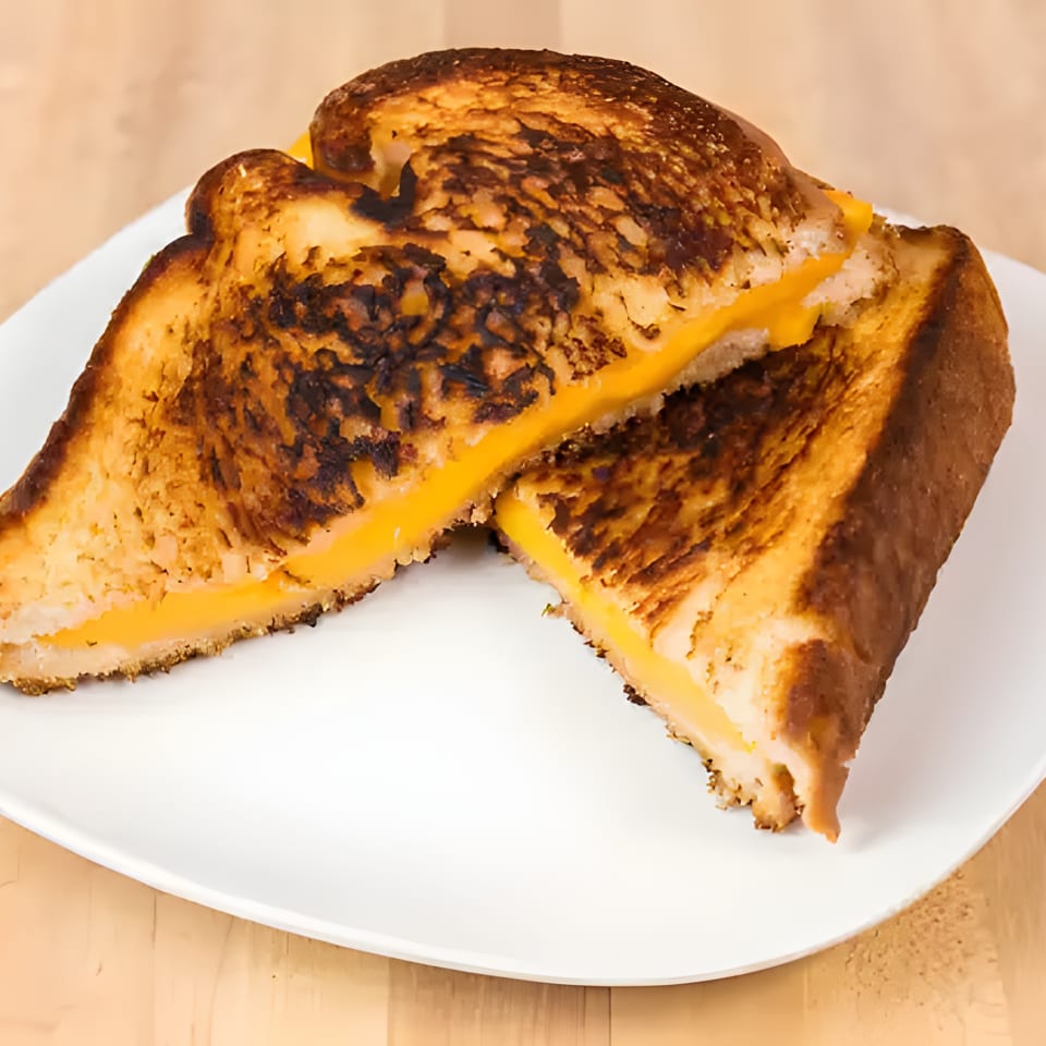 Two halves of a grilled cheese sandwich with melted orange cheese on a white plate.