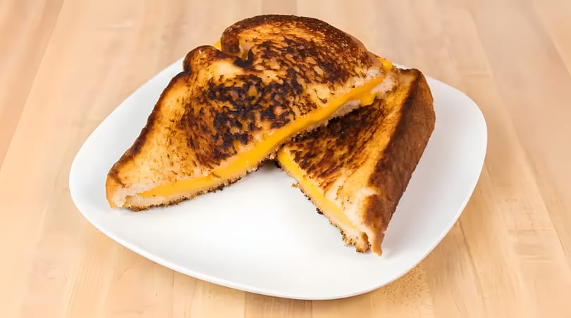 Two halves of a grilled cheese sandwich with melted orange cheese on a white plate.