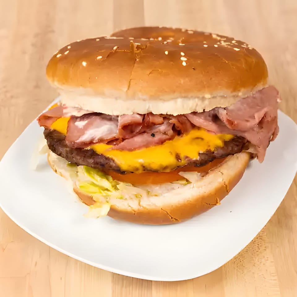 A large burger with cheese, bacon, lettuce, and tomato on a white plate.