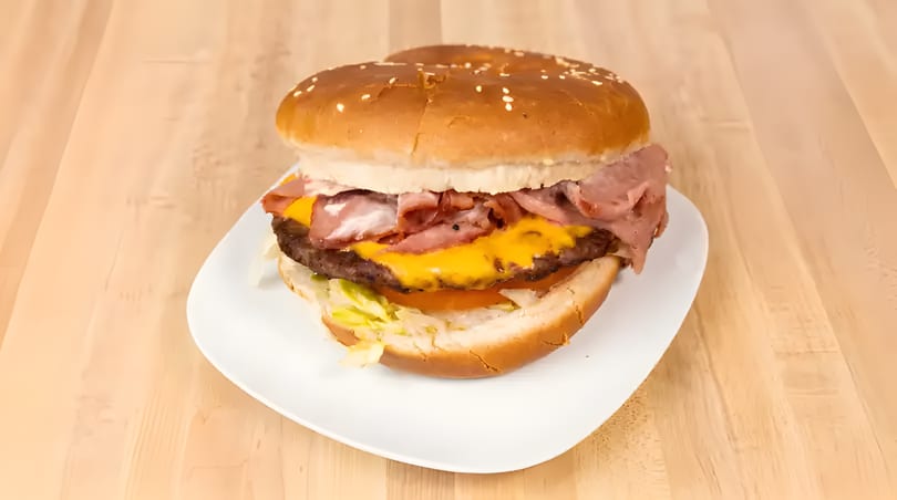 A large burger with cheese, bacon, lettuce, and tomato on a white plate.