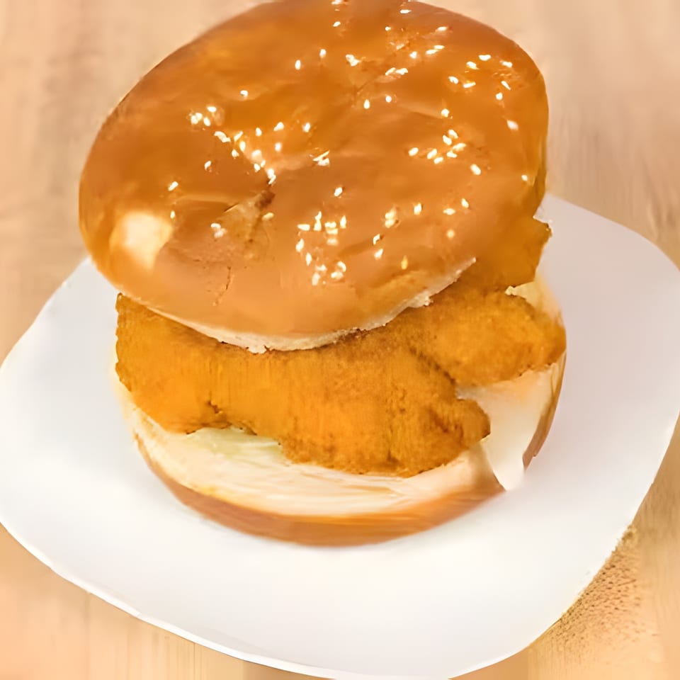 Crispy chicken sandwich on a sesame seed bun with lettuce and sauce, served on a white plate.