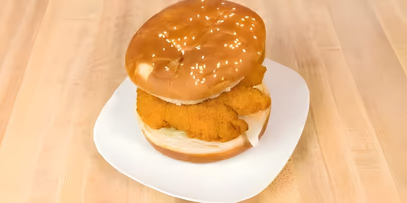 Crispy chicken sandwich on a sesame seed bun with lettuce and sauce, served on a white plate.