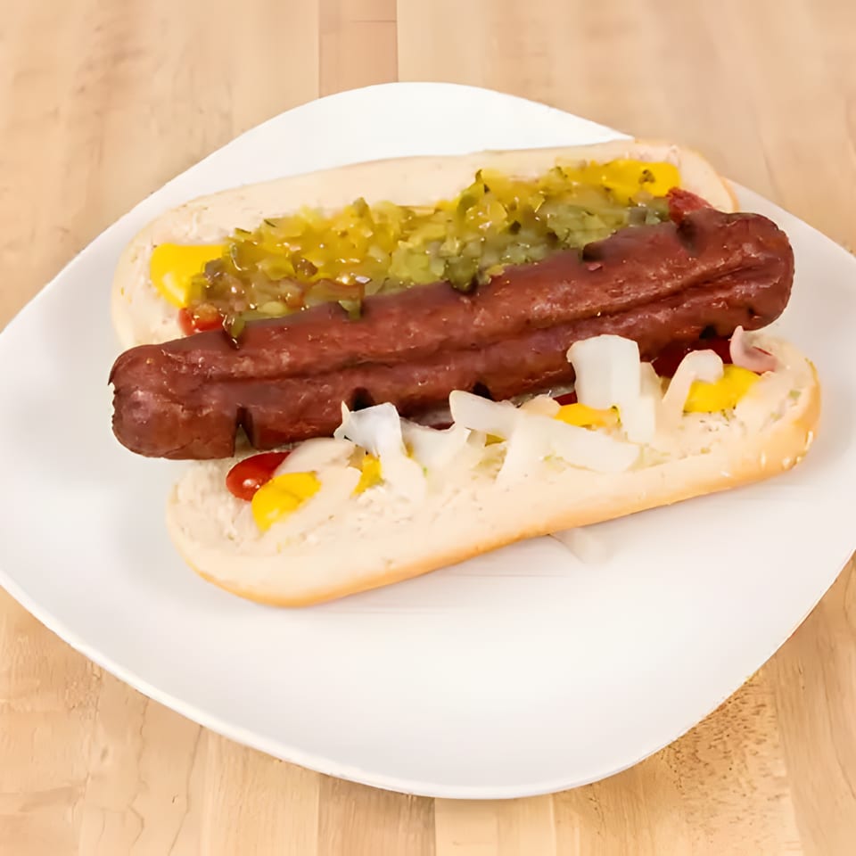 Two hot dogs with mustard, relish, and onions on a white plate on a wooden table.