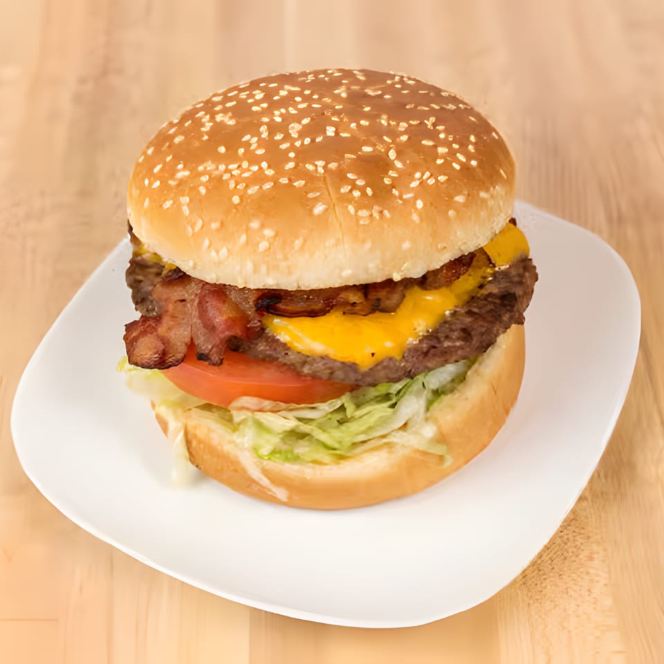 A bacon cheeseburger with lettuce and tomato on a sesame seed bun, served on a white plate.