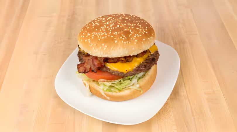 A bacon cheeseburger with lettuce and tomato on a sesame seed bun, served on a white plate.